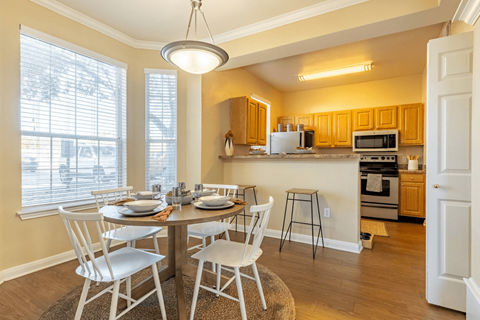 a dining area with a table and chairs and a kitchen in the background