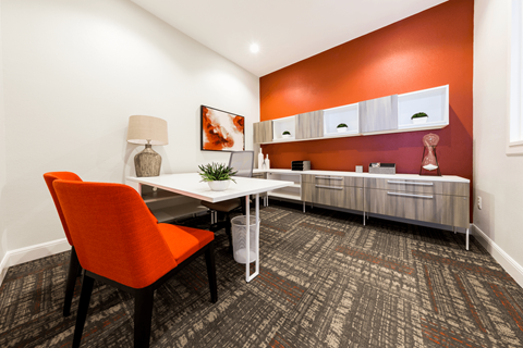 a desk and chair in a room with a red accent wall