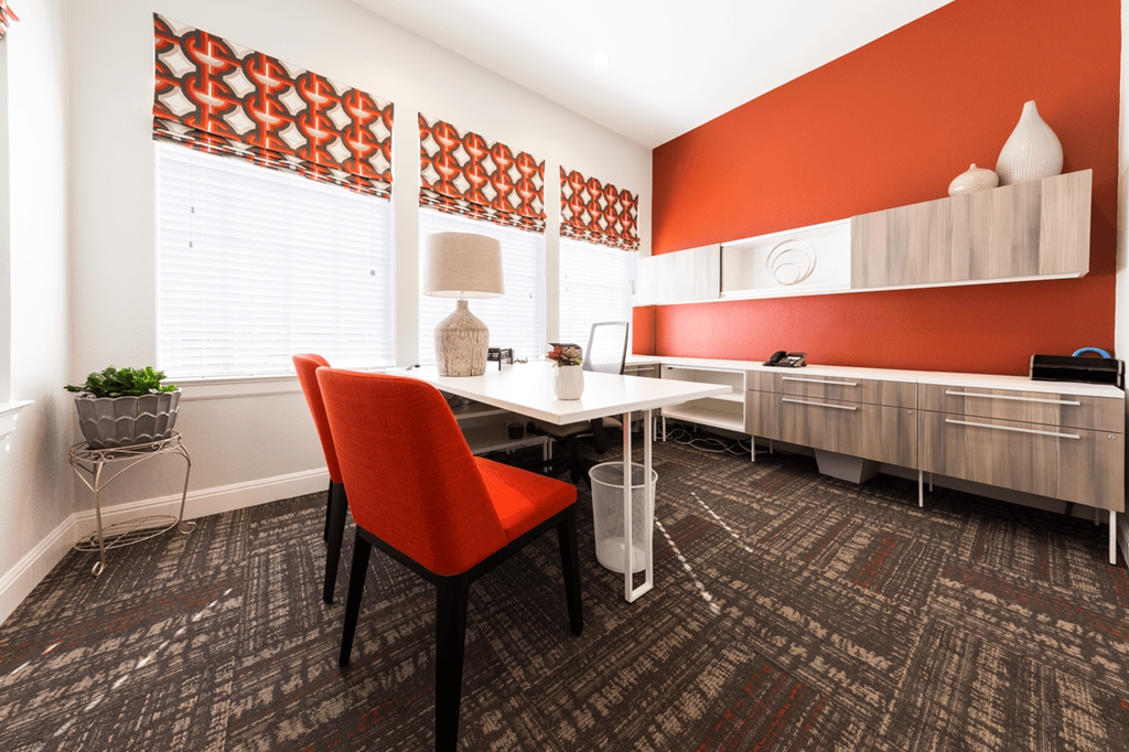 a desk with a chair and a lamp in a room with red walls and carpeting