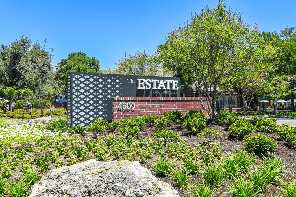 a sign that says the estate in front of a brick wall with trees in the background