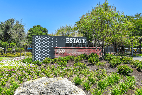 a sign that says the estate in front of a brick wall with trees in the background