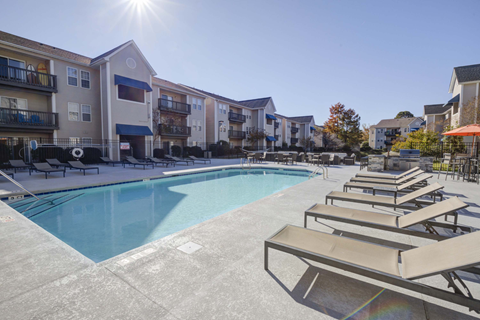A sunny day at the pool with lounge chairs and apartment buildings in the background.
