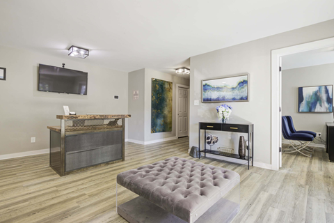 A living room with a grey tufted ottoman in the center.