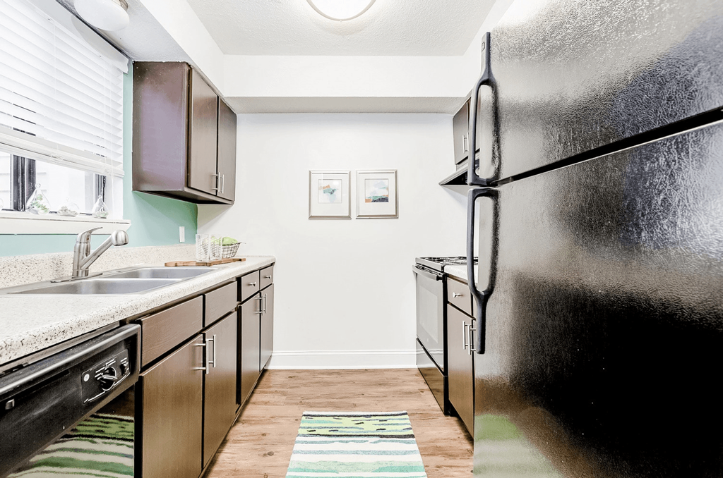 A black refrigerator stands in a kitchen with wooden floors and white walls at Regency Park Apartment Homes, Raleigh, North Carolina