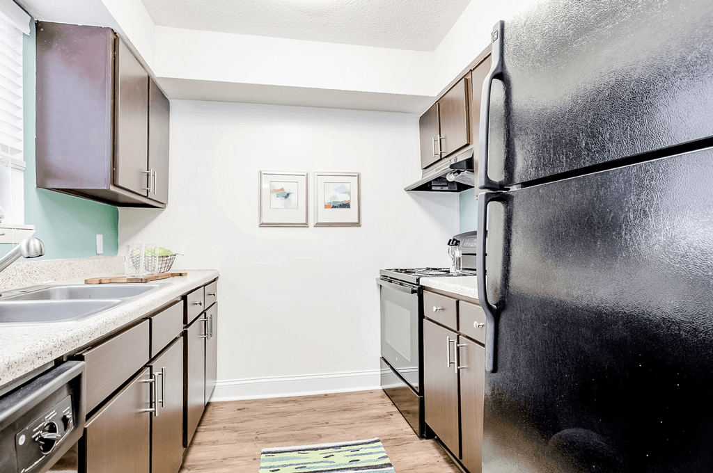 A black refrigerator stands in a kitchen with wooden cabinets and a white counter. at Regency Park Apartment Homes, Raleigh, North Carolina