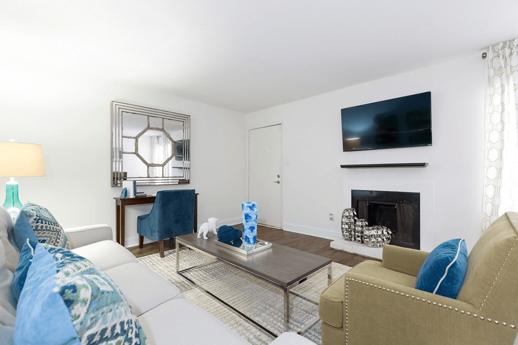 A living room with a white couch, a tan armchair, a glass coffee table, and a fireplace at Regency Park Apartment Homes, Raleigh, North Carolina