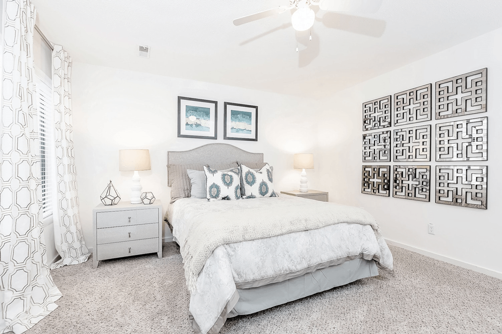 A bedroom with a large bed, a ceiling fan, and a wall of framed pictures at Regency Park Apartment Homes, North Carolina