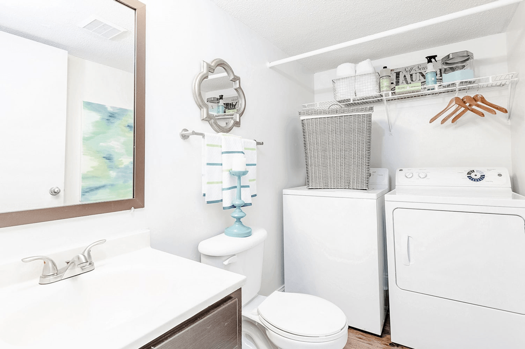 A white bathroom with a toilet, sink, and washing machine at Regency Park Apartment Homes, Raleigh
