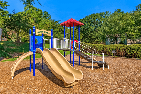 A playground with a yellow slide and a red roofed structure.