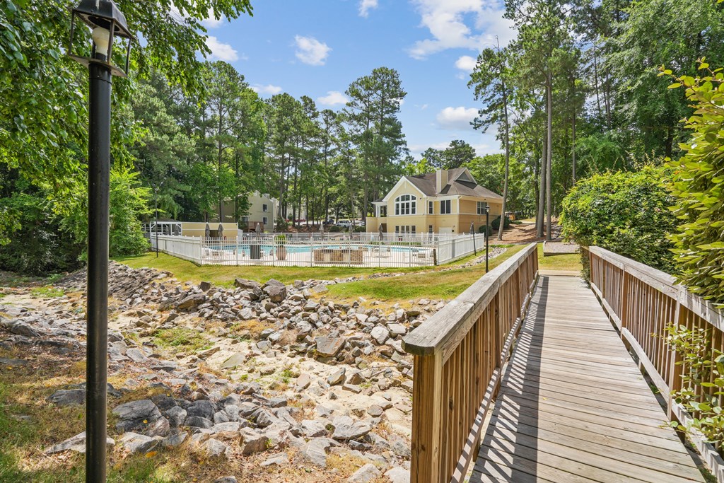 A wooden walkway leads to a house with a pool in the foreground at Regency Park Apartment Homes, Raleigh