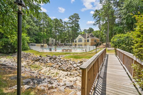 A wooden walkway leads to a house with a pool in the foreground.