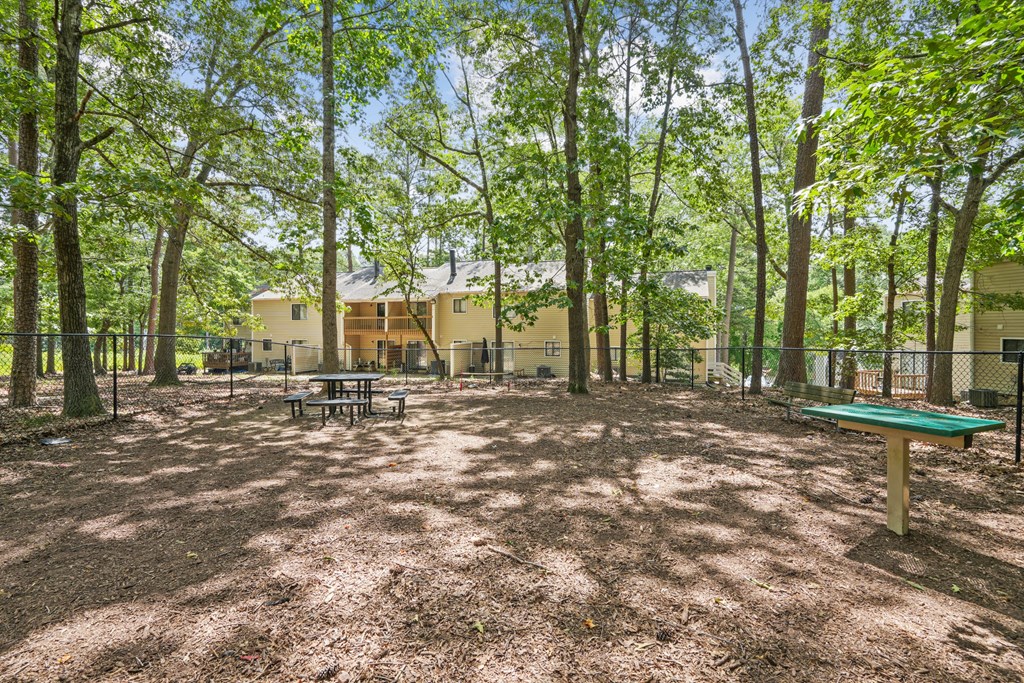 A playground with a green table and a picnic table surrounded by trees at Regency Park Apartment Homes, Raleigh, 27616