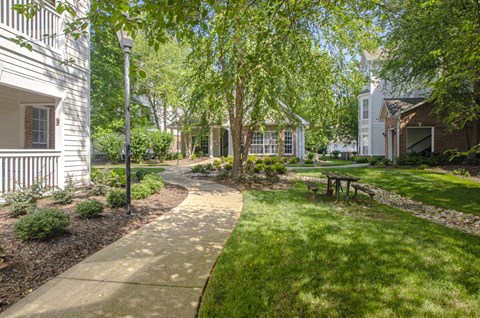 a pathway through a grassy area with trees and buildings in the background