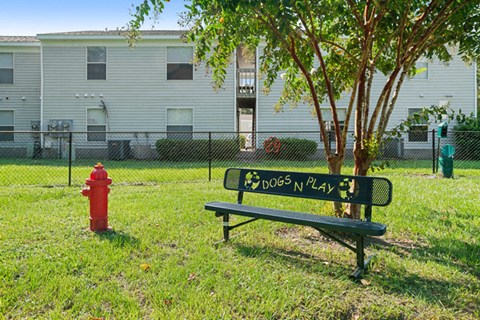 a bench and a fire hydrant in a grassy area with a building in the background