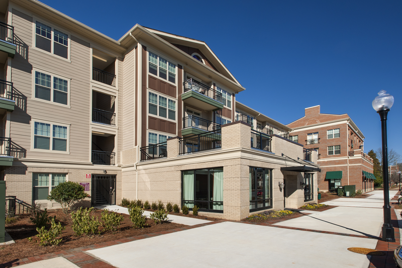 Exterior view of apartment buildings with trees and bushes lining a sidewalk