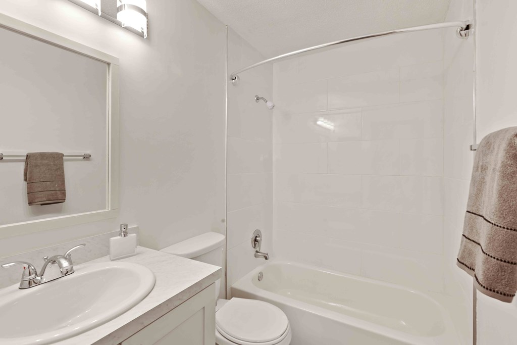 A white bathroom with a towel hanging on the shower rod.