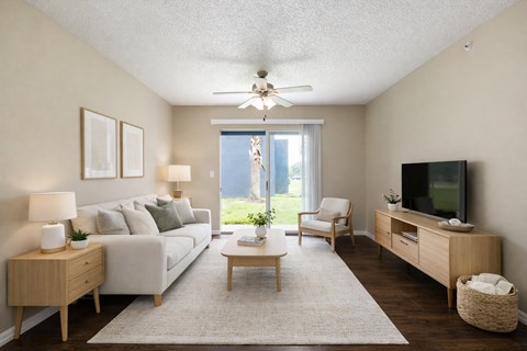A living room with a white couch, a wooden coffee table, a flat screen TV, and a ceiling fan.