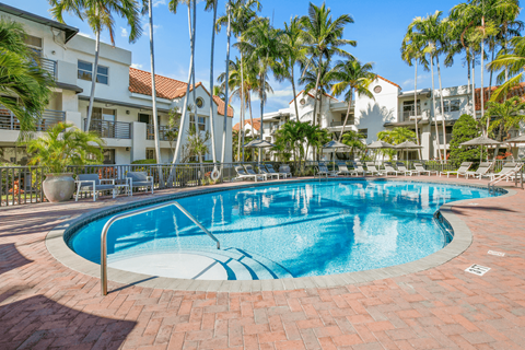 a resort style swimming pool with lounge chairs and palm trees in the background