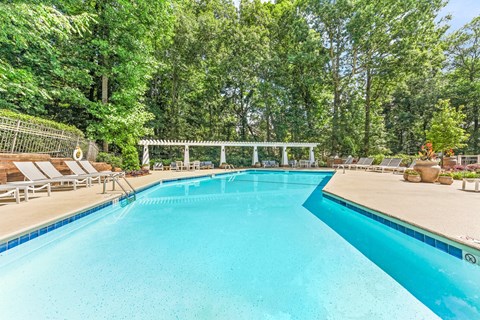 A large swimming pool surrounded by trees and lounge chairs.