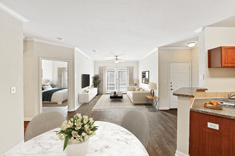 A well-lit, spacious living room with a kitchen area and a dining table set with a vase of flowers.