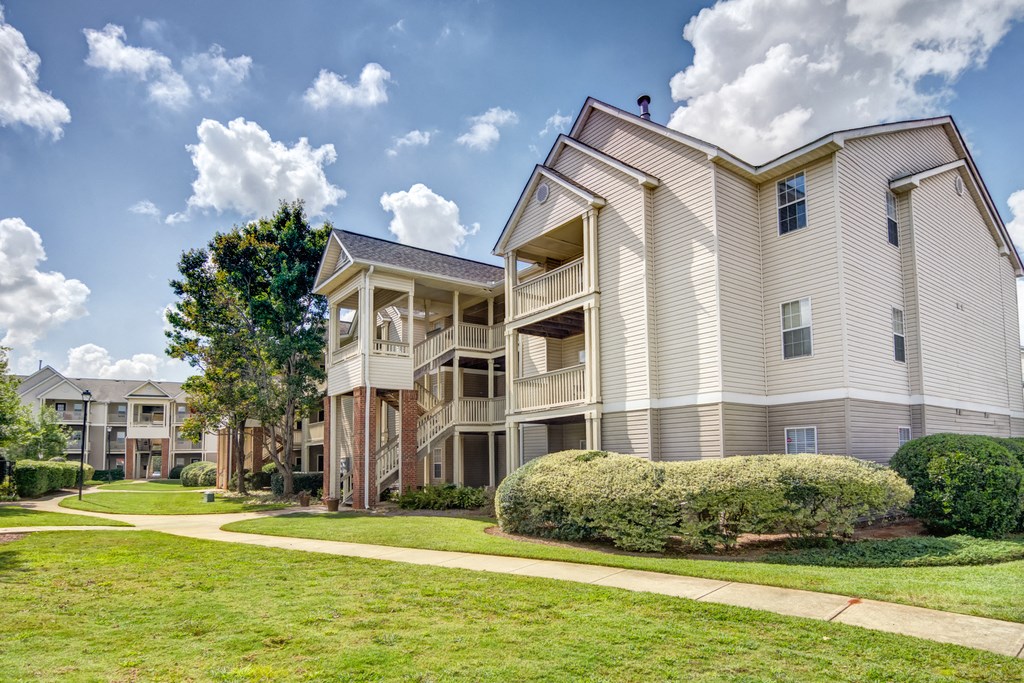Exterior of buildings with grass and trees and sidewalk leading into community.