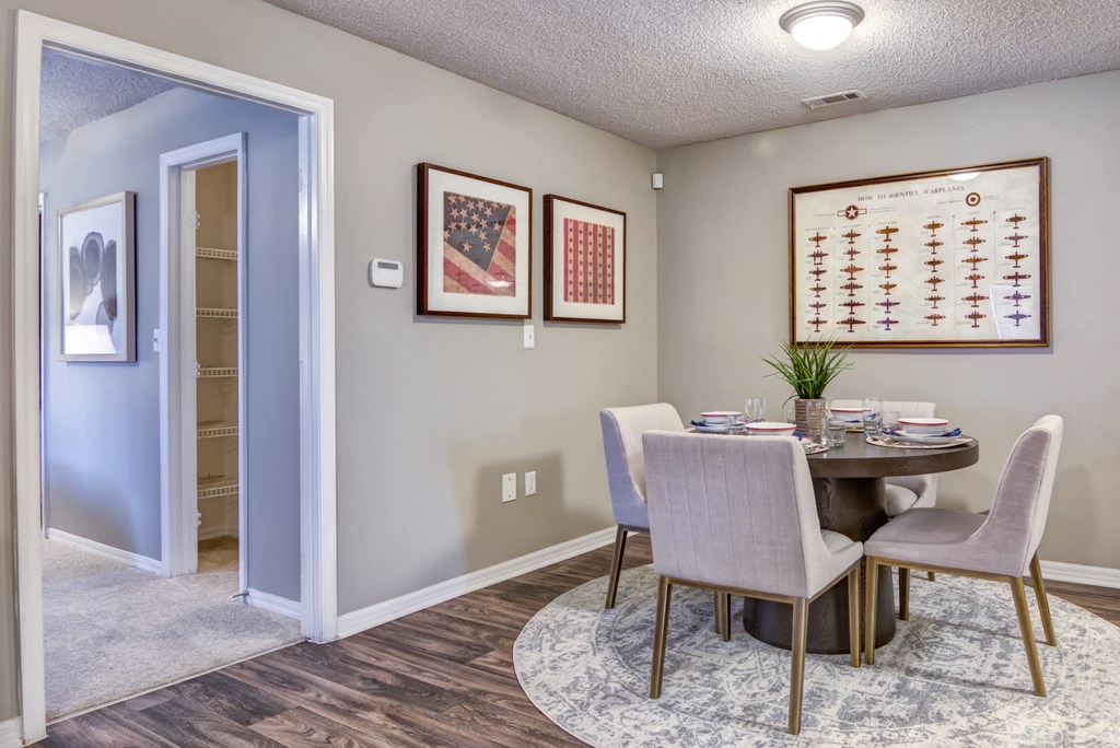 Staged dining room with gray walls, wood style flooring, a table with for chairs, decorative rug, and wall art.