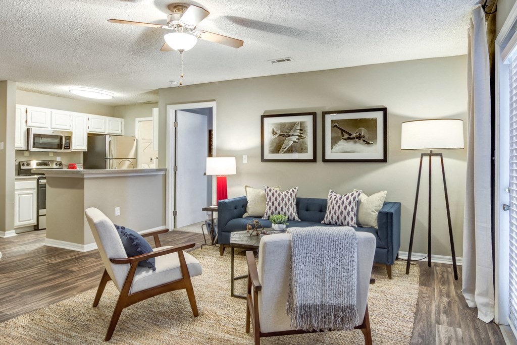 Staged living room with gray walls, wood style flooring, blue sofa, two gray accent chairs, decorative rug, coffee table and wall art.
