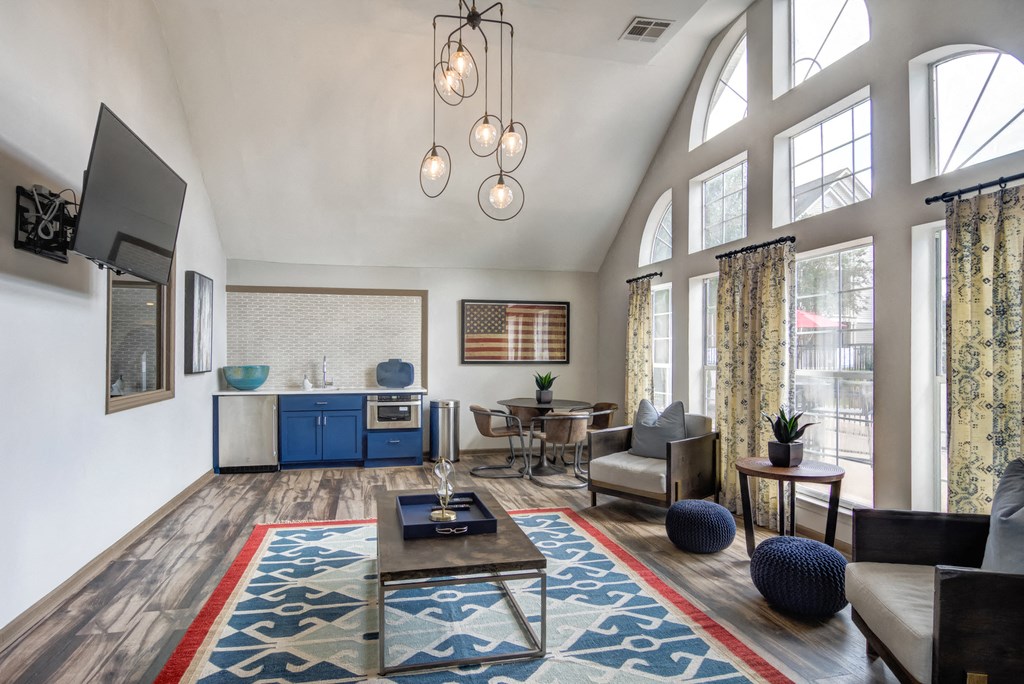 Clubhouse with two decorative chairs, a coffee table, decorative rug, wall mounted television, a table with four chairs and kitchen.