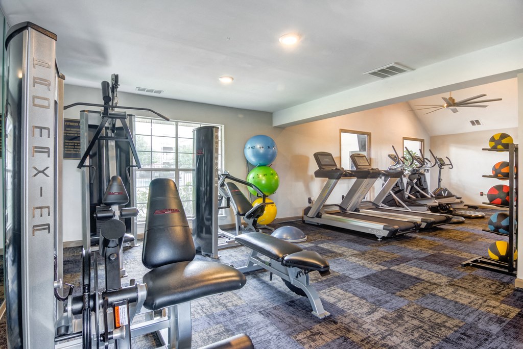 Fitness center with exercise equipment, large window, and ceiling fan.