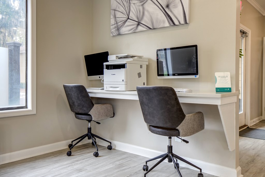 Two black chairs are placed in front of a desk with a monitor and a printer on it.