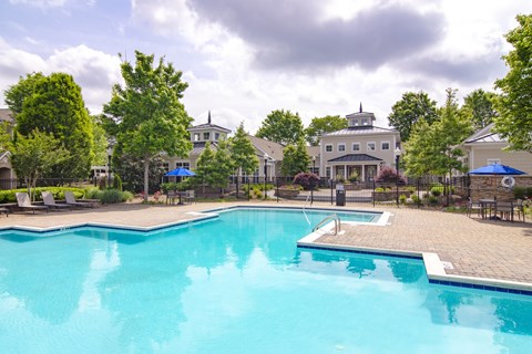 A large swimming pool surrounded by trees and a building in the background.