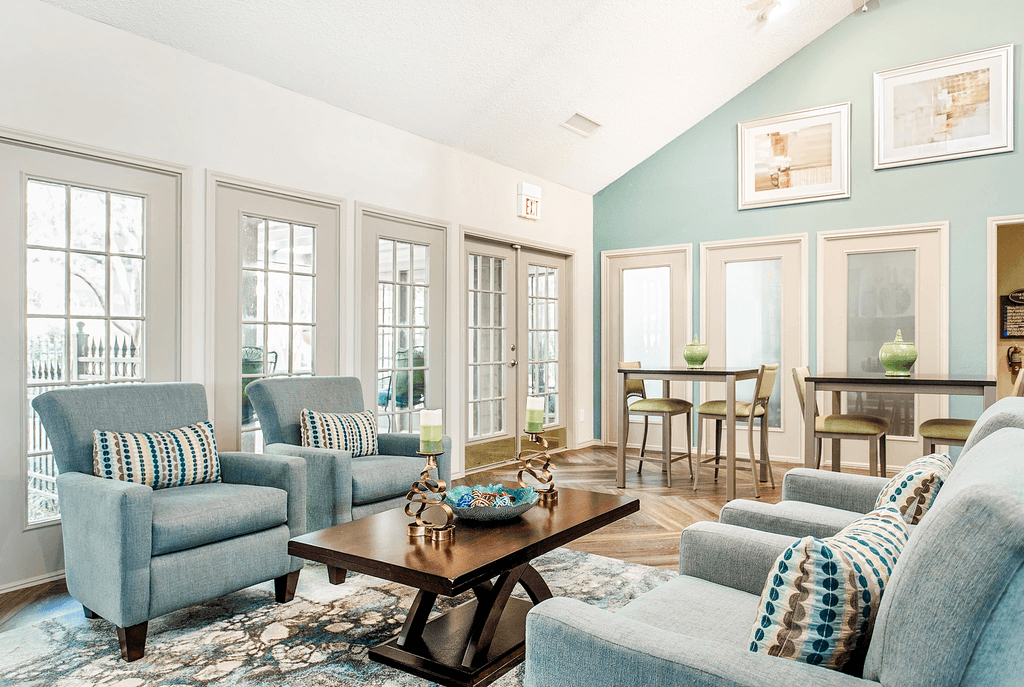 Clubhouse interior with upholstered chairs, accent rug, coffee table, high top tables and chairs, vaulted ceiling and ceiling fan
