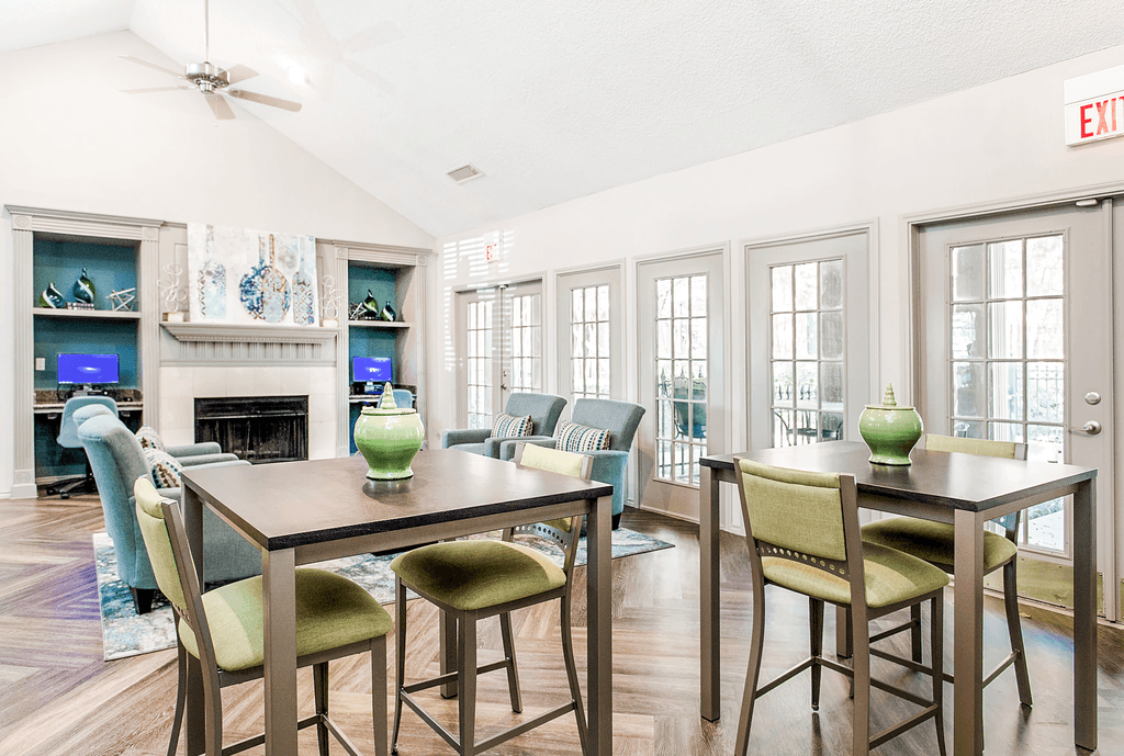 Clubhouse interior with high top tables and chairs, wood style flooring, fireplace with mantel, doors and windows, vaulted ceiling and ceiling fan