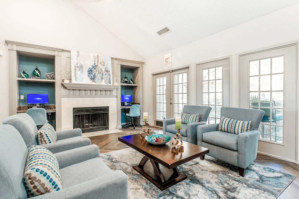 Clubhouse interior with upholstered chairs, accent rug, coffee table, vaulted ceiling, fireplace with mantle and computer desks with chairs and computers