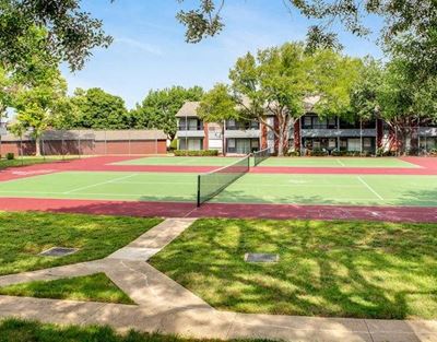 tennis court with apartment buildings in the back ground with trees