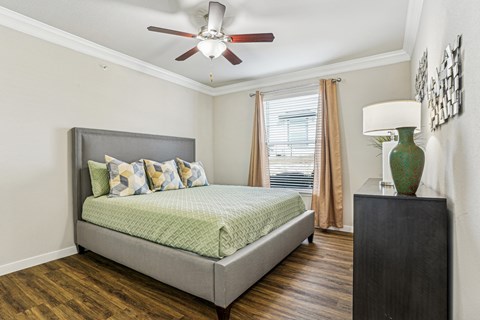 A bedroom with a bed, a ceiling fan, and a wooden floor.