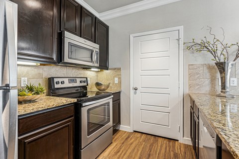 A kitchen with a white door and a black microwave above the stove.