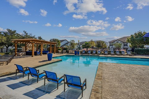 A pool area with blue chairs and a wooden pergola.