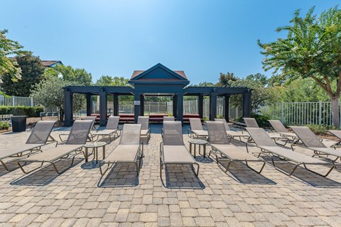 A gazebo is surrounded by lounge chairs on a brick patio.