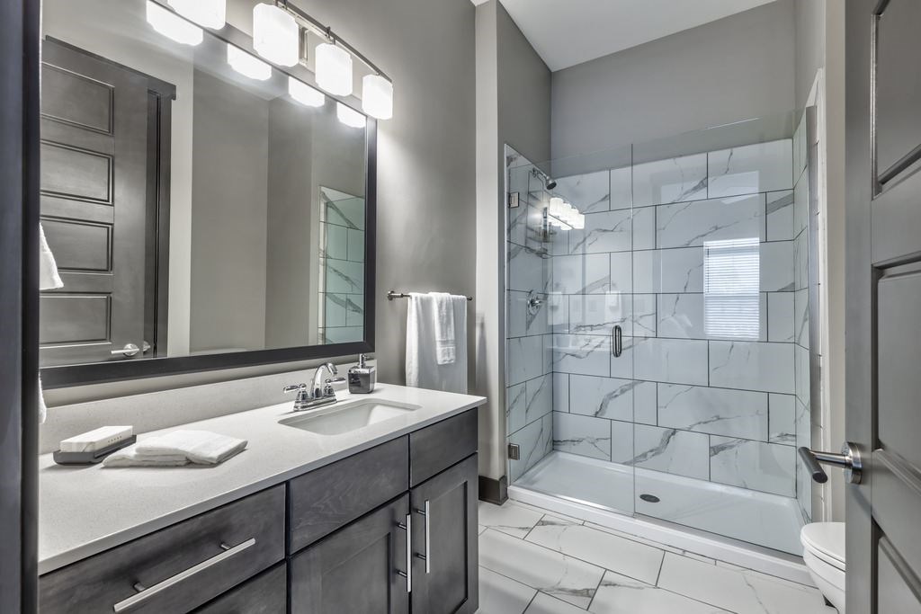 A modern bathroom with a marble tile shower and a large mirror above the sink.