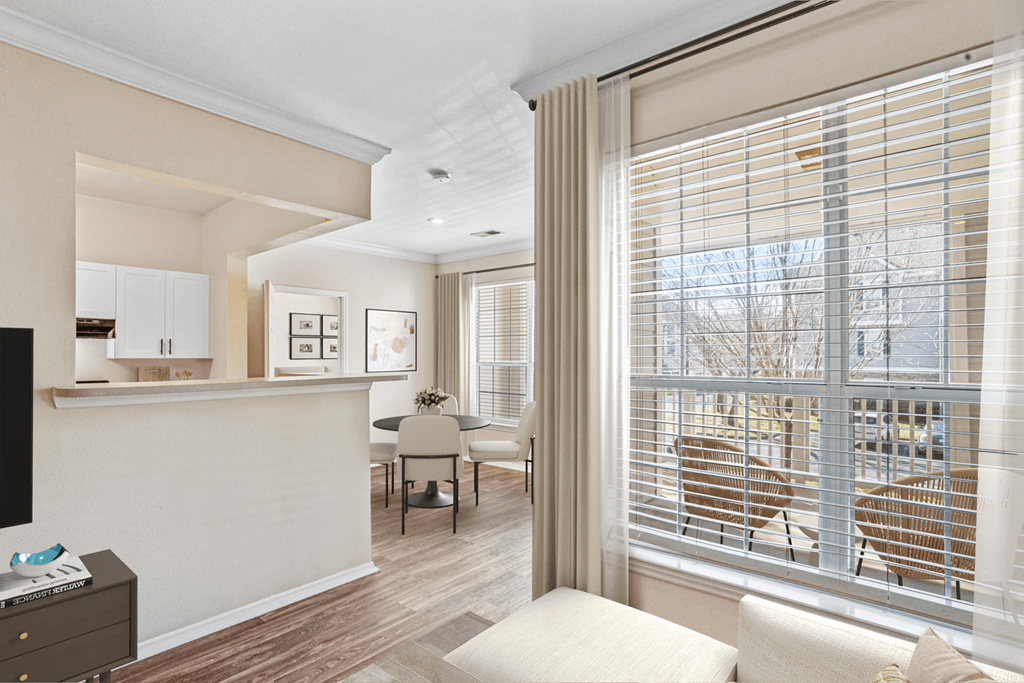 a living room with a large window and a dining room in the background