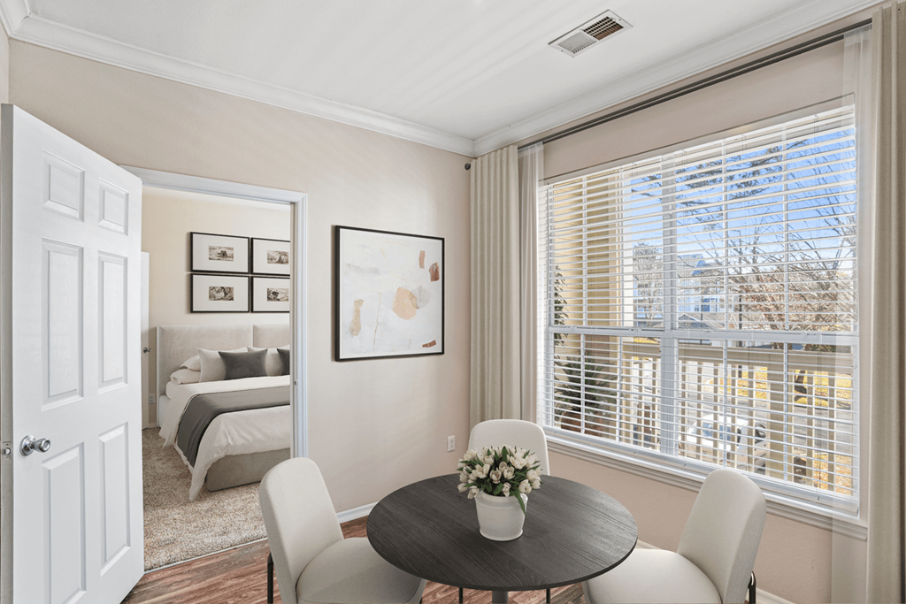 a dining area with a table and four chairs and a large window with blinds