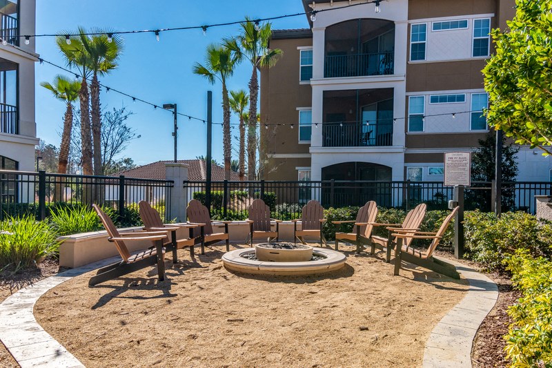 an outdoor seating area with chairs and a fire pit in front of an apartment building