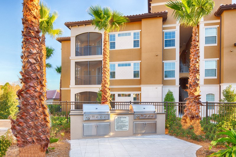 two gas barbecue grills in front of an apartment building with palm trees