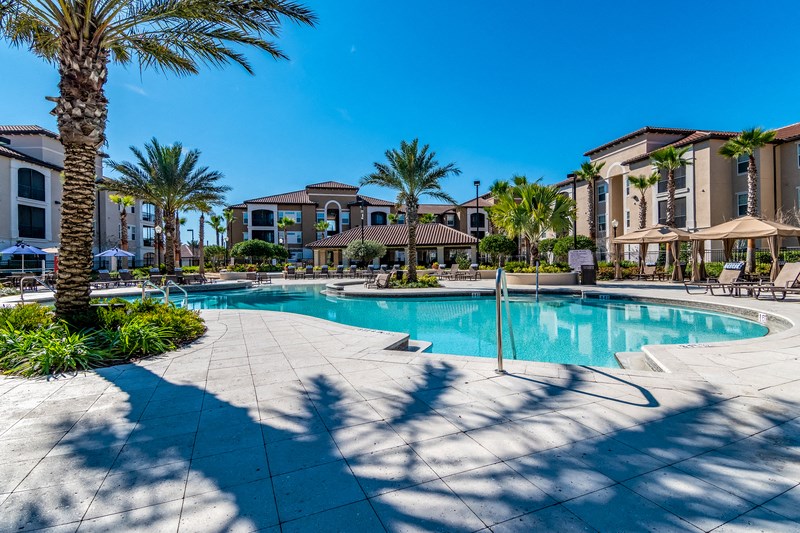 a swimming pool with palm trees and apartments in the background