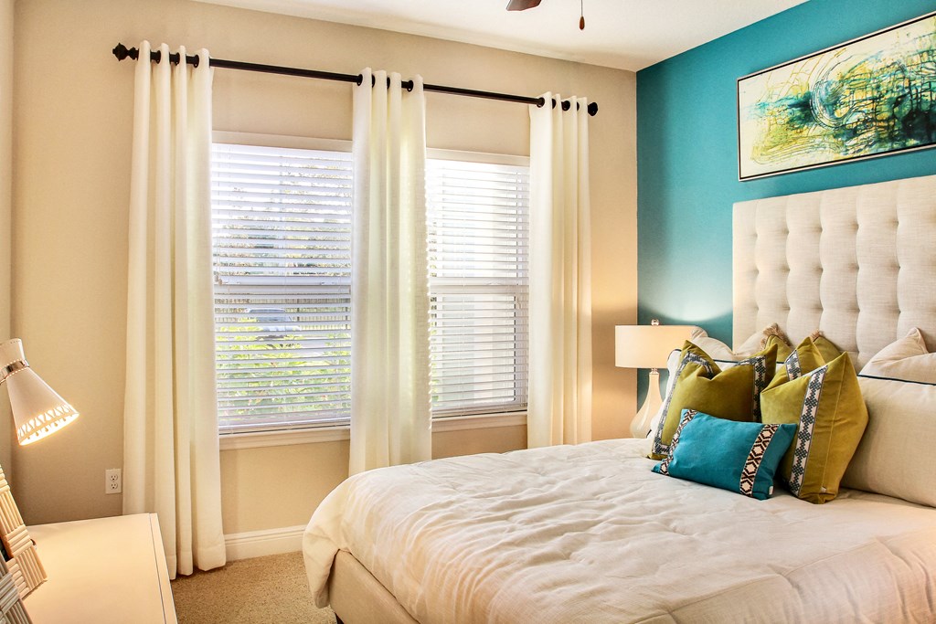 a bedroom with a bed and two windows with white curtains