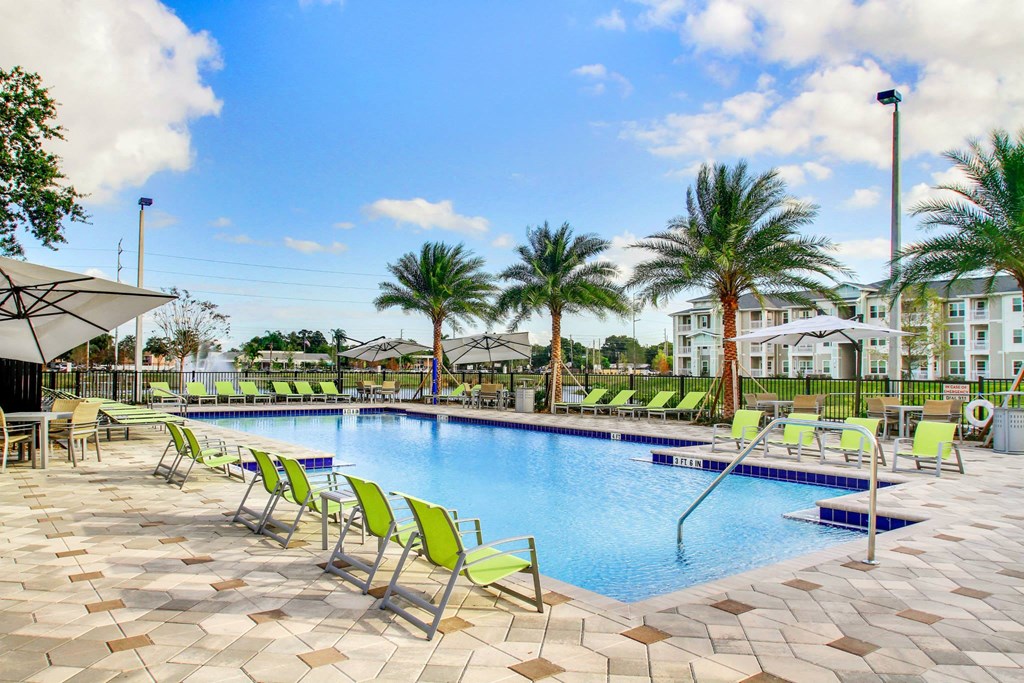 a swimming pool with green chairs and palm trees