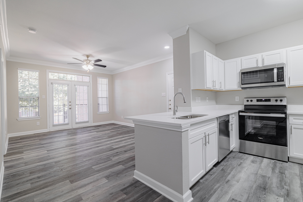 kitchen with stainless appliances, white cabinetry, and hardwood style flooring with living room in the background