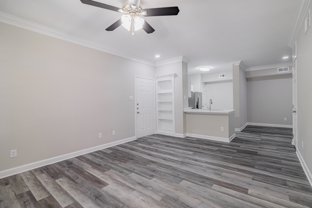 an empty living room with a ceiling fan and built-in shelving