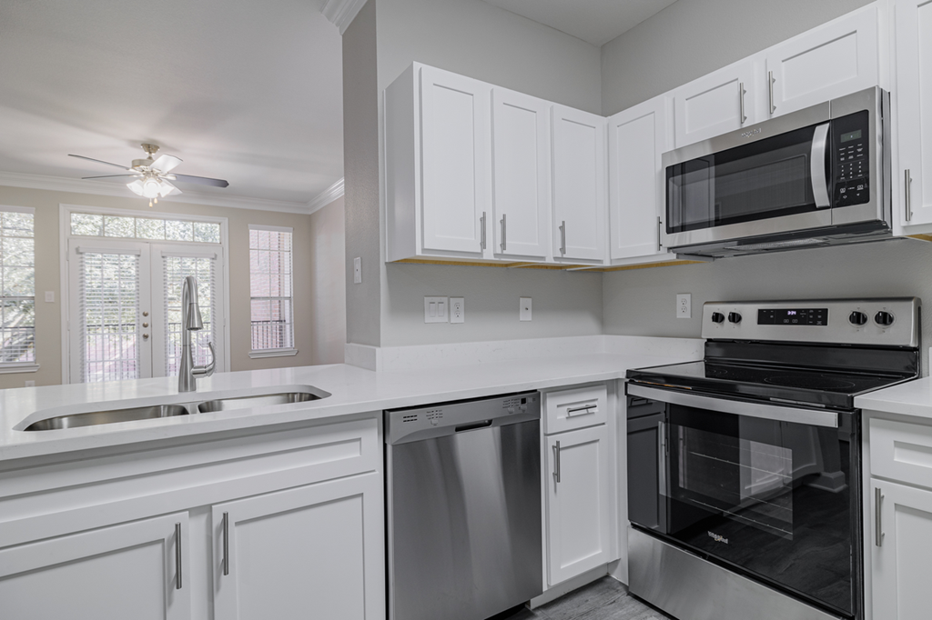 kitchen with stainless appliances, white cabinetry, and hardwood style flooring with living room in the background